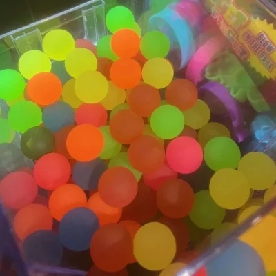Assorted 49mm frosty hi-bounce balls in neon green, orange, yellow, pink, and blue inside arcade prize machine bin