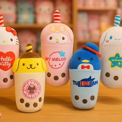 Five Sanrio character-themed boba plush toys, including Hello Kitty, My Melody, and Tuxedosam, are displayed on wooden tables inside a pastel-colored Japanese kawaii shop. The blurred background features plush toys and accessories neatly arranged on wooden shelves, creating a warm and playful retail atmosphere.