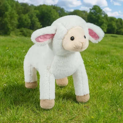 Plush lamb toy standing on green meadow grass with trees and blue sky in the background.