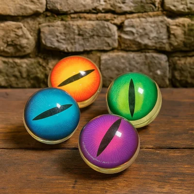 A fair-skinned hand holds a green dragon eye bouncy ball in front of a weathered stone castle wall, bathed in warm ambient lighting.