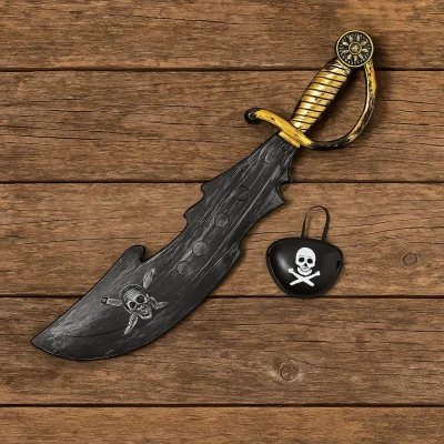 Black plastic pirate sword with gold hilt and matching skull-and-crossbones eye patch resting on rustic wooden planks.