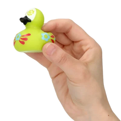 Hand Image: "Hand holding a green Day of the Dead themed rubber duck with floral and heart decorations, black beak, and colorful patterns against a white background."