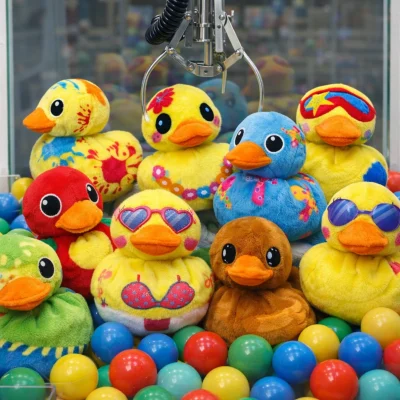 7-inch assorted plush ducks displayed inside a claw machine on top of colorful plastic balls, with a metal crane hanging above the prize pile.
